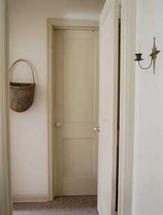 an empty hallway with a basket hanging on the wall and another door in the background