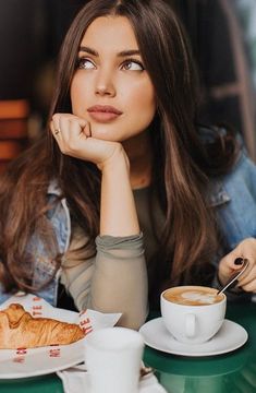 a woman sitting at a table with a cup of coffee and croissant in front of her