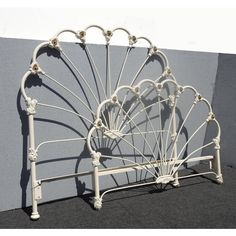 a white metal bed frame against a gray wall with decorative iron work on the headboard