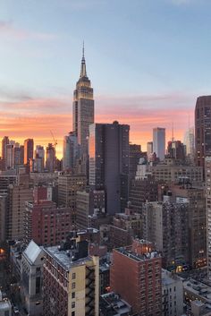 the sun is setting over new york city, with skyscrapers in the foreground