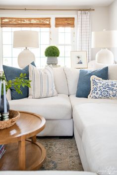 a living room with white couches and blue pillows on the back of the couch