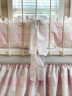 a baby crib with pink and white checkered bedding, bow on top