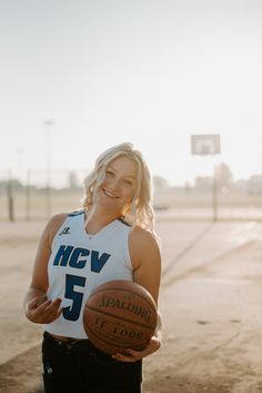 a woman holding a basketball in her right hand and smiling at the camera, while standing on a basketball court