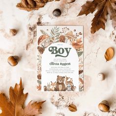 a baby shower book surrounded by leaves and acorns on a marble surface with the word boy written in green