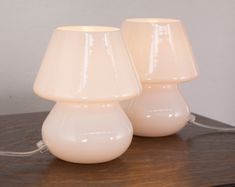 two white lamps sitting on top of a wooden table next to each other and one is turned off