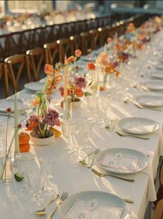 a long table is set with white plates and place settings for an elegant dinner party