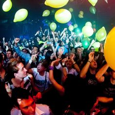 a large group of people at a party with balloons in the air and one person holding up a yellow balloon