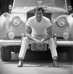 a man sitting in front of a car with his feet on the license plate,