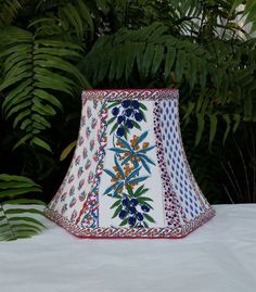 a lamp shade sitting on top of a table next to some plants and trees in the background