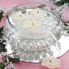 some white candles are in a glass bowl