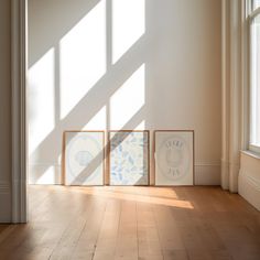 three framed art pieces sitting on top of a hard wood floor next to a window