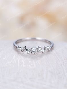 a three stone diamond ring sitting on top of a white cloth covered table with flowers in the background