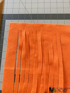 an orange piece of paper with some cut up strips next to it on a cutting board