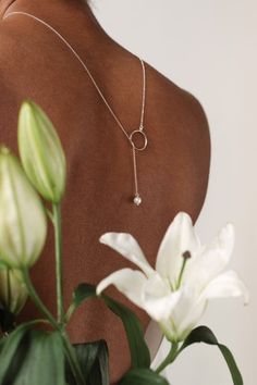 the back of a woman's neck with a necklace and flowers in front of her