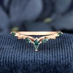 a gold ring with green stones and leaves on the front, sitting on top of a blue cloth