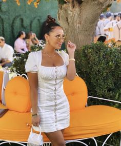 a woman in a white dress is talking on her cell phone while standing next to an orange couch