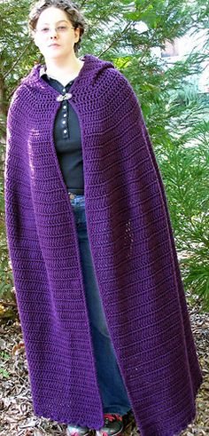 a woman wearing a purple crocheted shawl standing in front of some trees