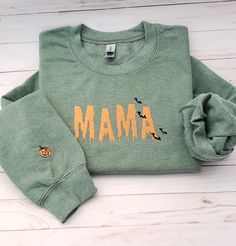 "Welcome to my store! This sweatshirt features an embroidered Spooky ooze font with the word \"mama\" in the middle of sweater, and a pumpkin on the right outer lower wrist. The thread color is orange but if you prefer a different color, kindly specify it in the personalization box. \"Stay cozy and stylish in this personalized embroidered sweatshirt! Made with high-quality material, this sweatshirt is designed to keep you warm and comfortable. The word 'mama' is beautifully embroidered on the front, making it a perfect gift for bridal showers or newlyweds.  This sweatshirt is perfect for a casual day out or a cozy night in. It comes in a range of sizes to fit anyone, and can be customized with your choice of trending hashtags to make it truly unique.  Make a statement with this mama sweats Green Fall Sweater With Embroidered Logo, Green Sweater With Embroidered Logo For Fall, Fall Green Sweater With Embroidered Logo, Green Embroidered Logo Sweater For Fall, Green Sweatshirt With Embroidered Logo For Fall, Long Sleeve T-shirt With Embroidered Logo For Fall, Halloween Embroidered Cotton Sweatshirt, Custom Embroidered Long Sleeve Top For Halloween, Embroidered Cotton Sweatshirt For Halloween