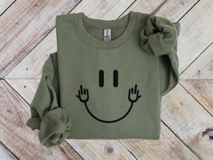 Stay warm and cozy with our Funny Middle Finger Sweatshirt, a perfect blend of comfort and humor! This Funny Smiley Face Sweater adds a playful twist to the classic happy face, making it a great choice for anyone with a fun sense of style. Whether you're lounging at home or out with friends, this Smiling Face Crewneck is perfect for those who love unique humor. Ideal as a Unique Humor T-Shirt for Teens or a Funny Party Happy Face Tee, it's sure to bring smiles and laughs wherever you go!   *Fast shipping in 2-5 Business Days! *Comfy unisex sweatshirts are soft and durable. *Measuring tip: Take your favorite sweatshirt or tee, lay it on a flat surface and measure the width (armpit to armpit) and length (top to bottom), then compare with our size chart. *Classic fit, durable and soft, poly/c Fun Crew Neck T-shirt For Loungewear, Funny Winter Streetwear Tops, Fun Long Sleeve Slogan T-shirt, Green Crew Neck Novelty Top, Fun Long Sleeve Slogan Tops, Fall Crew Neck Sweatshirt With Smiley Face, Funny Winter Top With Text, Fun Crew Neck T-shirt For Winter, Fall Smiley Face Crew Neck Sweatshirt