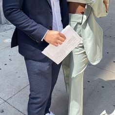 two people standing next to each other in front of a building wearing suits and ties