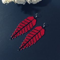 red and black beaded feather earrings next to white flowers