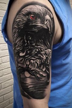 an eagle with red eyes on his arm is shown in this black and grey tattoo