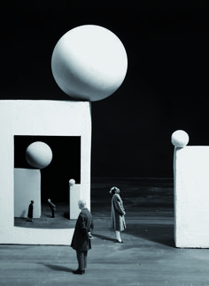 black and white photograph of two people standing in front of an abstract structure with large balls on top