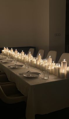 a long table with many lit candles on it and plates in front of the table