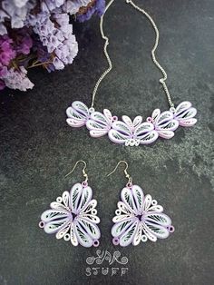 two pieces of jewelry sitting on top of a table next to some purple and white flowers