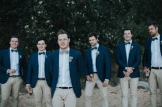 a group of men standing next to each other wearing suits and bow ties on the beach