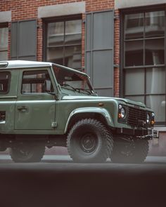 a green land rover parked in front of a brick building on a city street next to tall windows