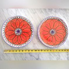 two orange plates sitting on top of a white counter next to a measuring tape and a ruler