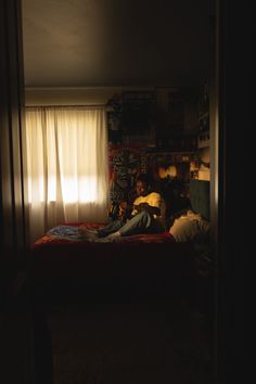 a man laying on top of a bed in a dark room next to a window