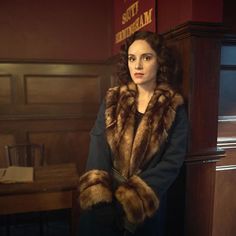 a woman in a fur coat leaning against a wall