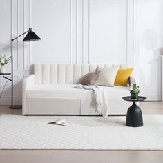 a white couch sitting on top of a wooden floor next to a lamp and table