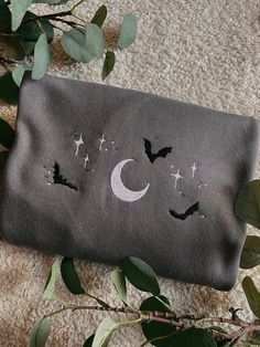 a gray bag with bats and stars on it sitting next to some green leaves in front of a white carpet