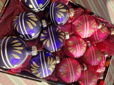 a box filled with purple and gold decorated christmas ornament's sitting on top of a striped table cloth