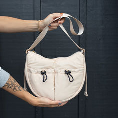 A super fun and comfortable trending shape of a bag! 

Made from our cloud material, with two exterior cinch pockets, one back zipper pocket that fits the largest iPhone, one interior zip pocket, and 2 interior mesh pockets.

This bag is perfect for everyday wear whether you want to wear it as a high shoulder bag, or a longer crossbody, it looks cool both ways!

Dimensions:
11" L x 8" H x 4" W
max strap length: approx 46 inch 
100% Nylon Exterior Cream Crossbody Bag, Cloud Material, Moon Bag, A Bag