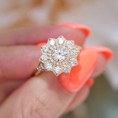 a woman's hand holding an orange manicured nail with a diamond ring on it