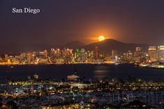 the full moon is setting over a city and bay in front of a large mountain