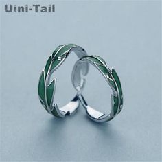 two silver rings with green leaves on the inside and outside, sitting on a blue surface