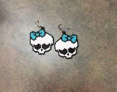 two beaded skull earrings with blue bows on them are sitting on the cement floor