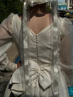 the back of a woman's wedding dress with white ribbons and flowers on it