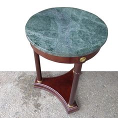 a green marble topped table on top of a wooden stand with brass trimmings