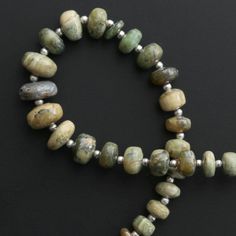 a beaded necklace with green and brown beads on a black surface, in the shape of an x