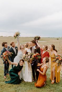 a group of people standing around each other in front of a grass field with flowers