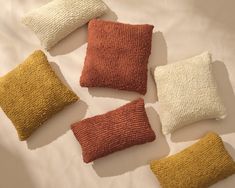 four different colored pillows sitting on top of a white bed spread with one orange and the other yellow