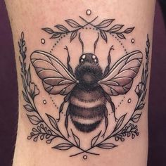 a black and white tattoo of a bee with leaves around it's perimeter on the leg