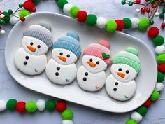 four decorated snowman cookies on a white platter