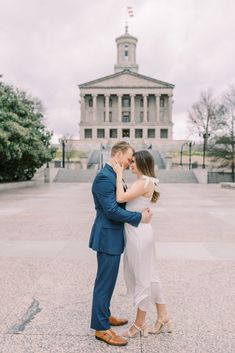 an engaged couple embrace in front of the state capitol building